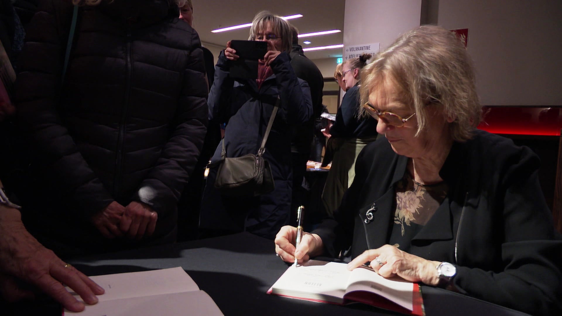 Elke Heidenreich sitzt an einem Tisch und signiert ein Buch. © Screenshot 