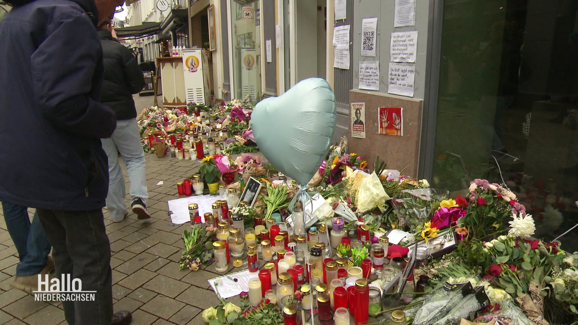 Blumen und Kerzen sind vor Schaufenstern auf dem Bürgersteig abgelegt und erinnern an einen getöteten jungen Mann. © Screenshot 