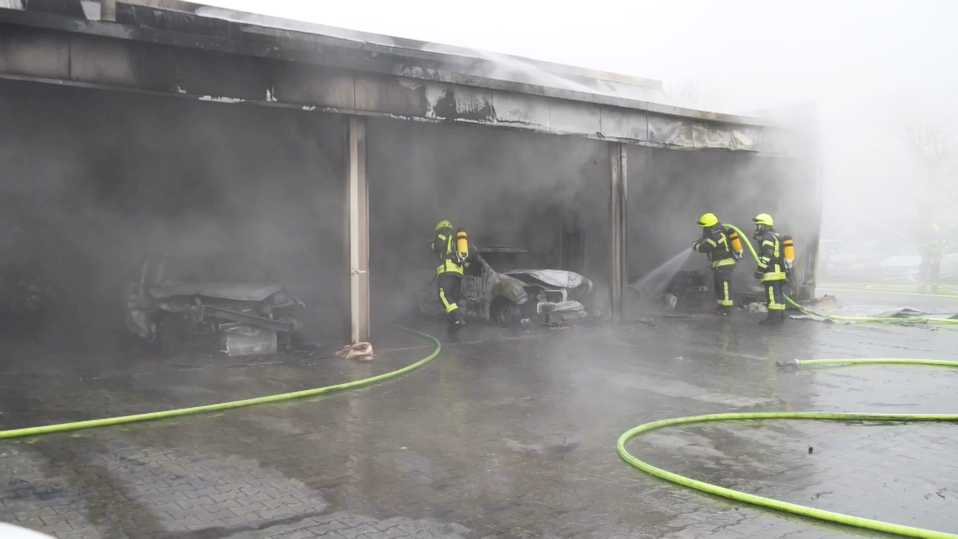 Zwei ausgebrannte Autos stehen unter einem Carport, drei Feuerwehrleute stehen mit Wasserschläuchen davor. Zwei ausgebrannte Autos stehen unter einem Carport, drei Feuerwehrleute stehen mit Wasserschläuchen davor. © TelenewsNetwork Foto: TelenewsNetwork
