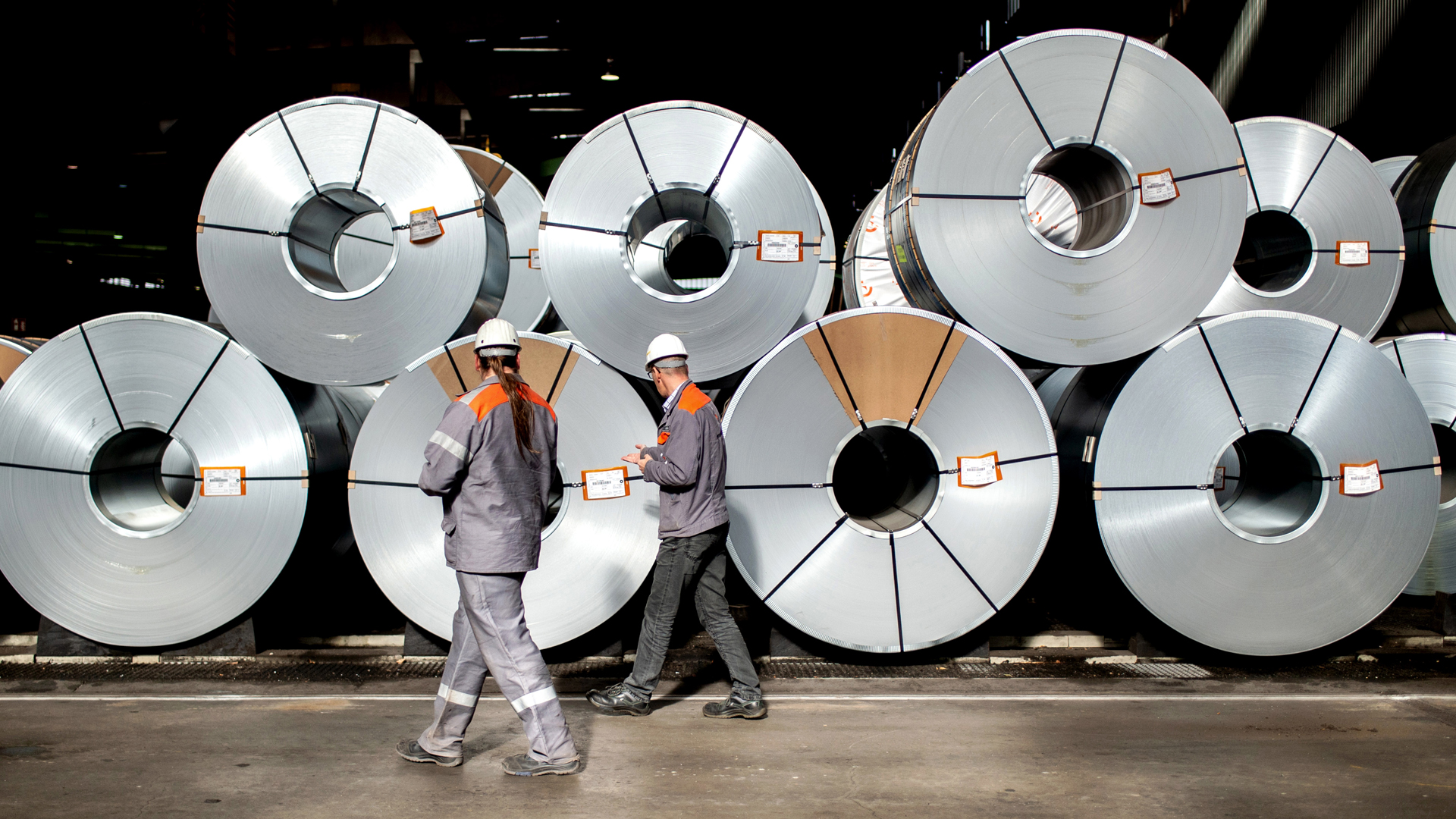 Zwei Mitarbeiter gehen vor aufgewickelten Metallbändern, sogenannten Coils, in einer Halle auf dem Gelände der Salzgitter AG entlang. © picture alliance/dpa Foto: Hauke-Christian Dittrich