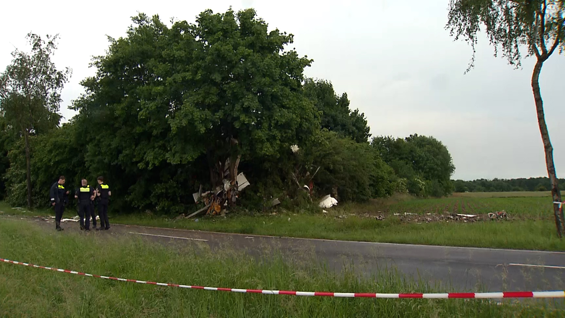 Trümmer eines Kleinflugzeugs sind in einer Baumgruppe zu sehen, Einsatzkräfte der Polizei stehen daneben. © NonstopNews 