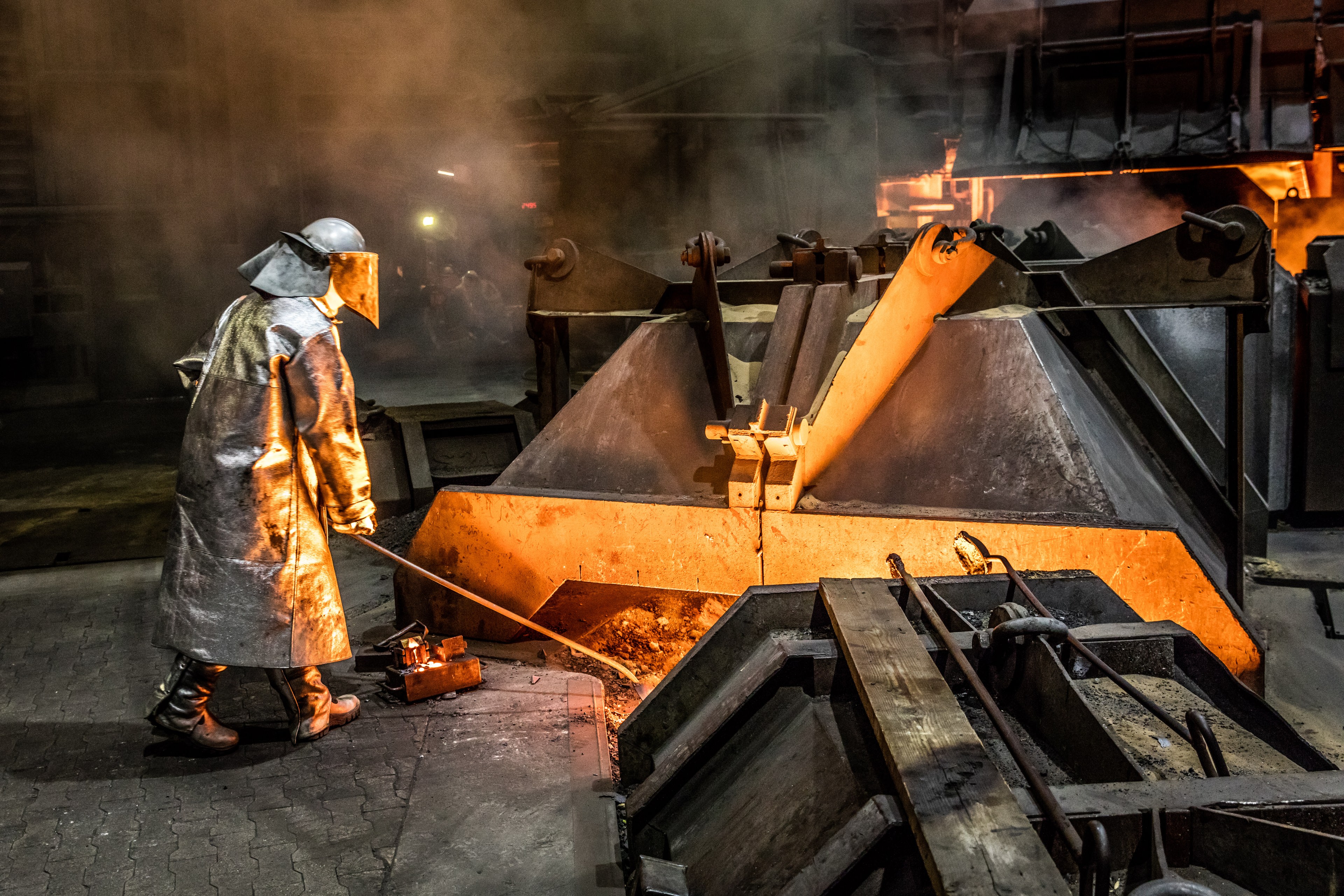 Ein Mitarbeiter der Salzgitter AG steht in Schutzkleidung vor einem Hochofen und entnimmt eine Roheisenprobe. © Salzgitter AG 