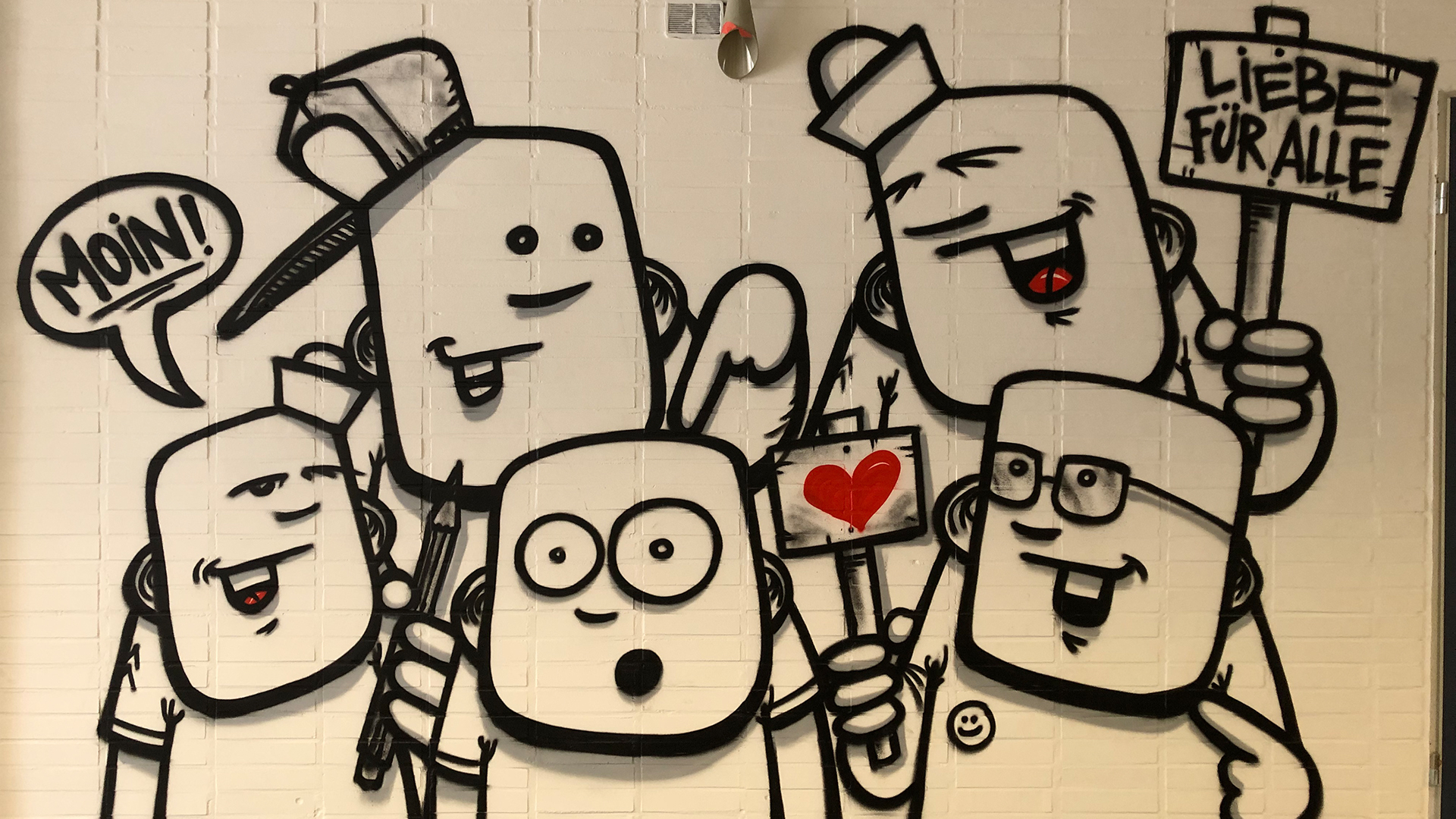 Ein modernes Graffitti mit jungen Leuten an einer weißen Wand. Eine Person hält ein Schild in der Hand mit der Aufschrift "Liebe für alle". © Grundschule Ellerau 