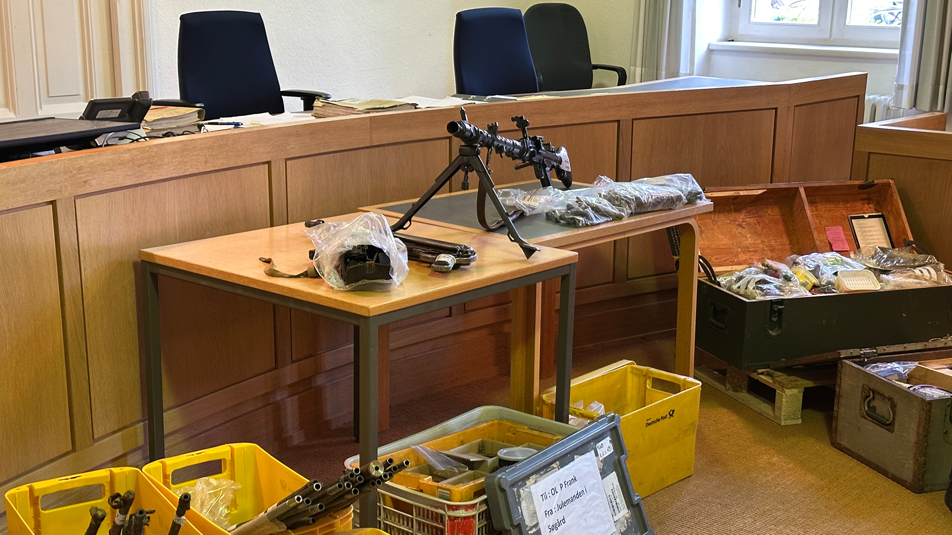 Eine Schusswaffe und Kisten mit weiteren Beweismitteln liegen in einem Gerichtssaal. © NDR Foto: Ben Armstrong