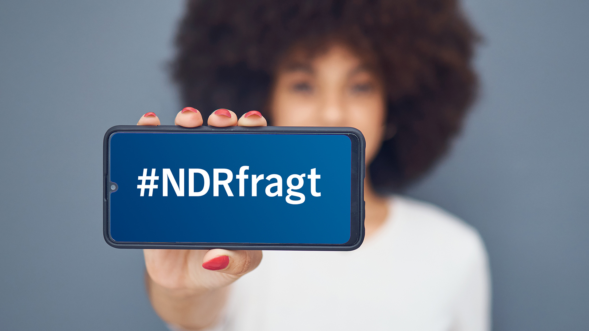 Eine Frau hält ein Smarthphone in die Kamera, auf dem Display steht "#NDRfragt" © PantherMedia Foto: Yuri Arcurs